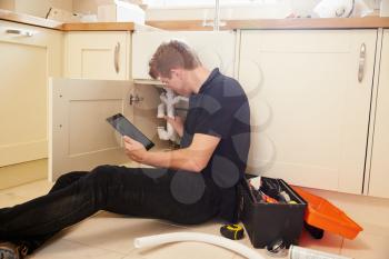 Plumber fixing sink in kitchen consulting tablet computer