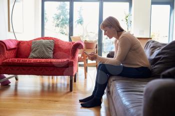 Woman Sitting On Sofa Sending Text Message On Phone