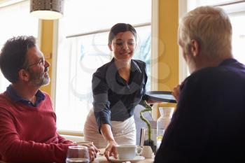 Waitress serving coffee to a male couple in a restaurant