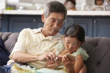 Grandfather And Granddaughter Using Mobile Phone At Home