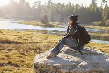 Young woman sits on a rock in countryside admiring the view