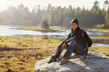 Young woman sits on a rock in countryside looking to camera
