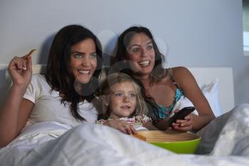 Young girl watching TV in bed with gay female parents