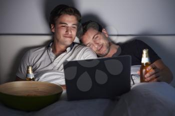 Man leaning on his boyfriend in bed, watching a laptop