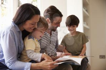 Family Sitting On Window Seat Reading Story At Home Together