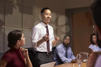 Asian businessman standing to address colleagues at meeting