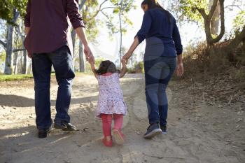 Parents and young daughter walk hand in hand on a rural path