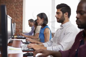 Staff Sitting At Desks Using Computers In Busy Office