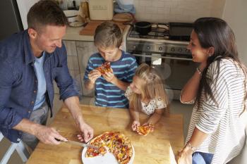 Family At Home In Kitchen Eating Homemade Pizza Together
