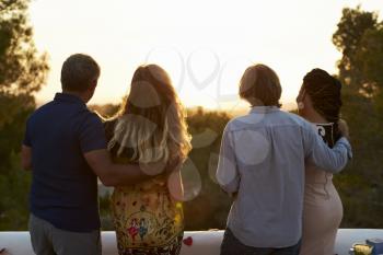 Two couples admire view from a rooftop at sunset, back view