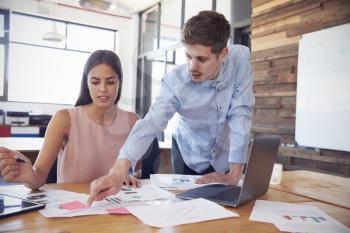 Young man stands working with a woman at her desk in office