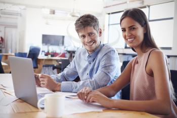 Young man and woman working in office smiling to camera