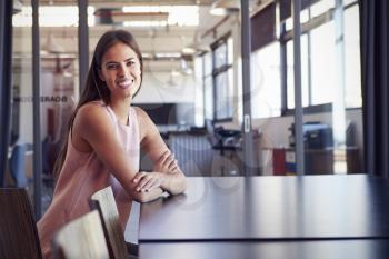 Young woman sitting alone in boardroom smiles to camera