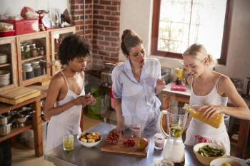 Three female friends making smoothies in kitchen