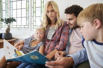 Family With Children Sitting On Bed Reading Book Together