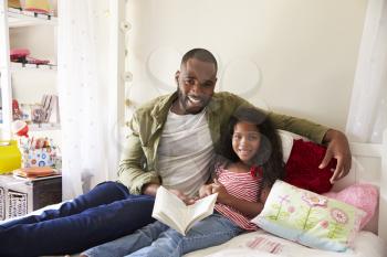 Portrait Of Father And Daughter Siting On Bed Reading Book