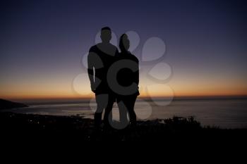 Couple standing by the sea at sunset on a beach, silhouette