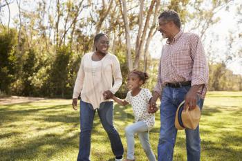 Grandparents And Granddaughter Walking In Park Together