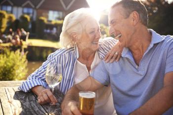Senior Couple Sitting At Table Enjoying Outdoor Summer Drink At Pub