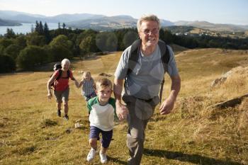 Grandparents With Grandchildren Climbing Hill On Hike Through Countryside In Lake District UK Together