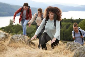 A multi ethnic group of young adult young adult friends smiling while climbing to a mountain summit, close up