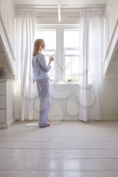 Woman Standing By Bedroom Window With Hot Drink