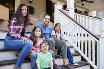 Family Sitting On Steps Of New Home On Moving In Day