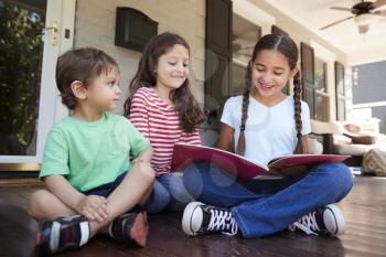 Group Of Children Sit On Porch Of House Reading Books Together