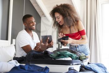Couple Looking At Digital Tablet As They Pack For Vacation