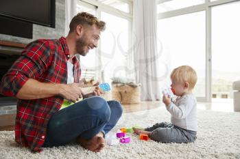 Father playing ukulele with young son at home, close up