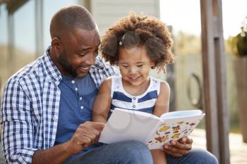 Young black father and daughter reading book outside