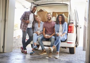 Friends Helping Couple To Unload Removal Truck On Moving Day