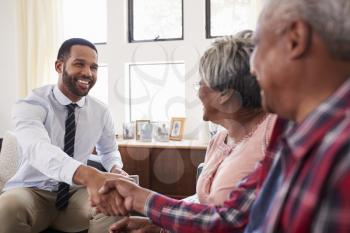Senior Couple Shaking Hands With Male Financial Advisor At Home