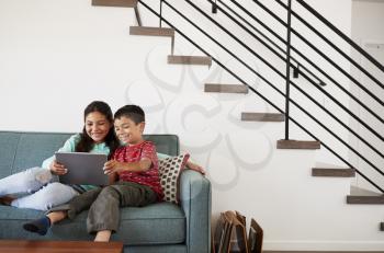 Brother And Sister Sitting On Sofa At Home Having Fun Playing On Digital Tablet Together