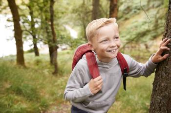Pre-teen boy taking a break leaning on a tree during a hike in a forest, elevated view, close up