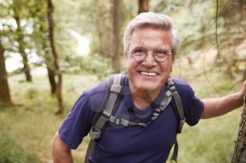 Middle aged Caucasian man taking a break leaning on a tree during a hike in a forest, smiling to camera, close up