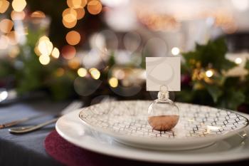 Close up of Christmas table setting with bauble name card holder arranged on a plate and green and red table decorations