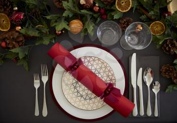Christmas table setting with a red Christmas cracker arranged on a plate and green and red table decorations, overhead view