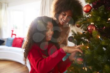 Mother And Daughter Hanging Decorations On Christmas Tree At Home