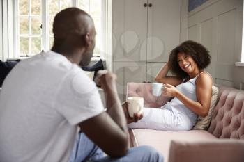 Young adult black woman sitting on a couch drinking coffee smiling at her partner, selective focus