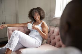 Young adult black couple sit drinking coffee looking at each other in the morning, over shoulder view, close up