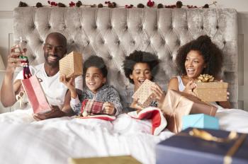 Young mixed race family sitting up in bed together holding presents on Christmas morning, front view, close up