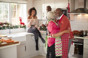 Multi-ethnic adult family celebrating  with champagne, talking and dancing in the kitchen while preparing dinner on Christmas Day