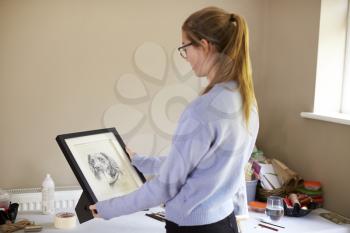 Female Teenage Artist Holding Framed Charcoal Drawing Of Dog In Studio
