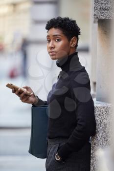 Young adult woman standing on a street in London using her smartphone and looking away, selective focus