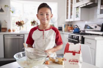 Proud pre-teen boy making cake mixture on his own in the kitchen, smiling, close up