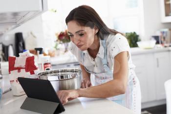 Millennial Hispanic woman preparing cake mixture checking the recipe on her tablet computer