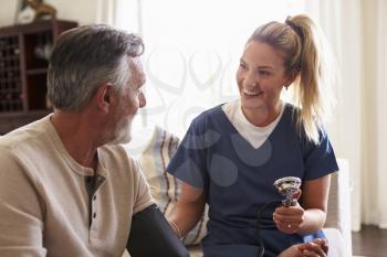 Female healthcare worker making home visit to a senior man, taking his blood pressure, close up