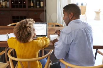 Back view of pre-teen girl sitting at a table in the dining room working on a laptop computer with her home tutor, close up