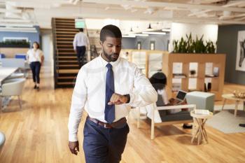 Businessman Walking Through Modern Office Checking Health Data On Smart Watch